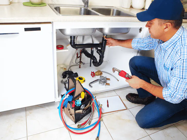 Emergency plumbing service beneath a kitchen sink