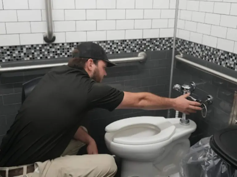 Plumber checking bathroom fixture connections during leak detection